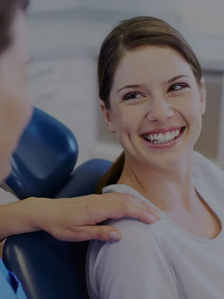 A smiling patient in a dental chair with a dental provider's hand resting on their shoulder.